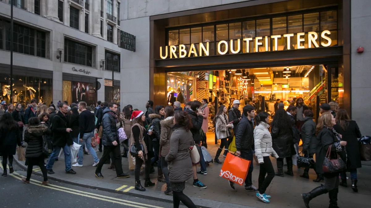 An Urban Outfitters storefront is pictured while a large amount of shoppers walk on the sidewalk in front of it.