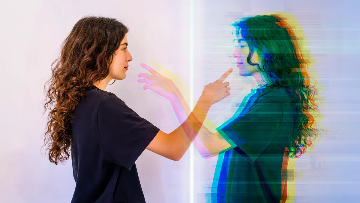 A young woman faces her digital twin, reaching out to make contact.