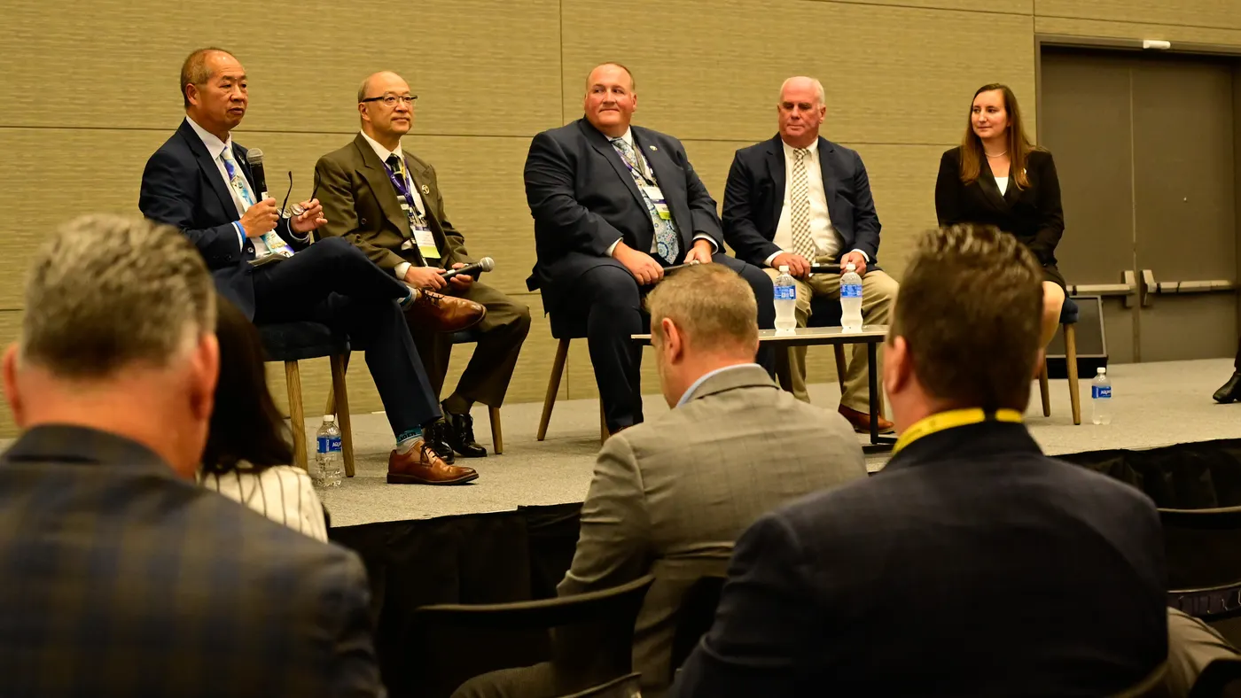 Four men in sutis and a woman on a stage with audience members in the foreground.