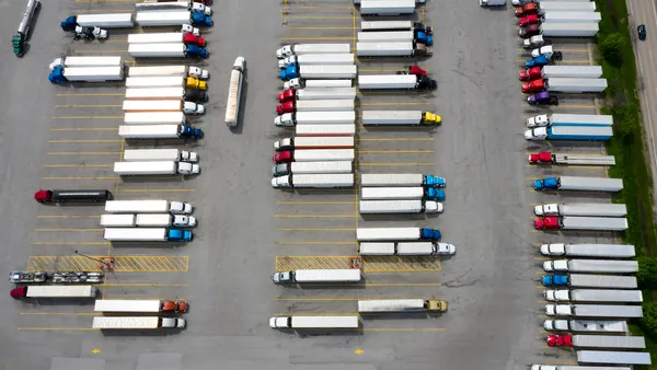 Aerial view of a large group of semi-trucks parked at a highway truck stop with scores of tractor-trailers present.