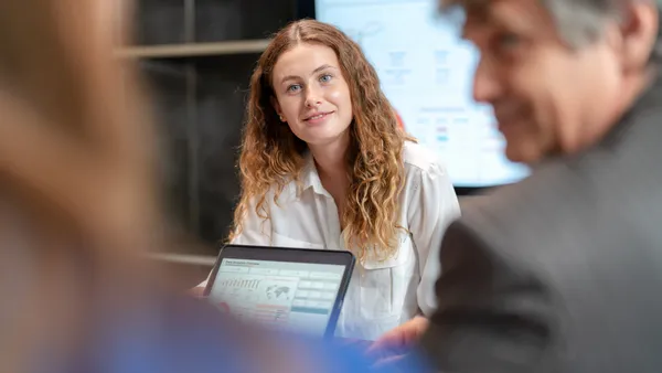 A businessperson shows a tablet with graphs on it to two other people.