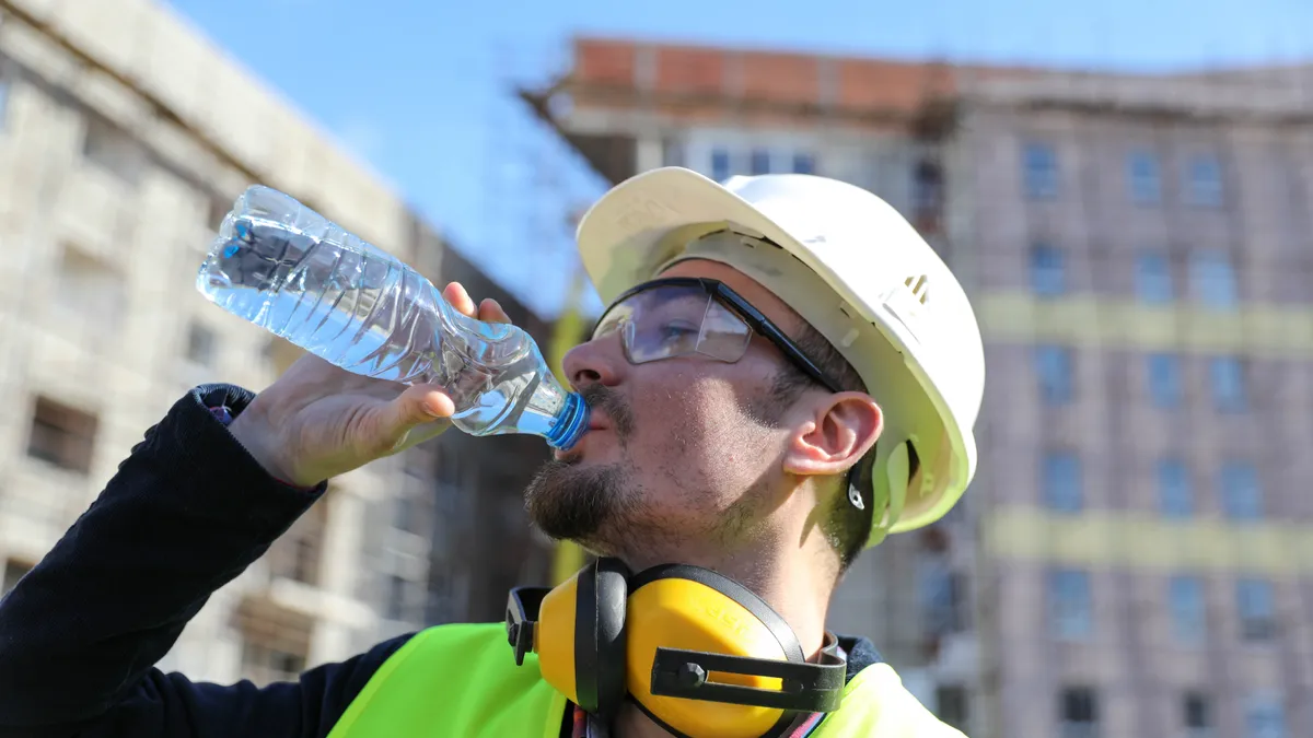 A construction worker in safety gear drinks from a water bottle.