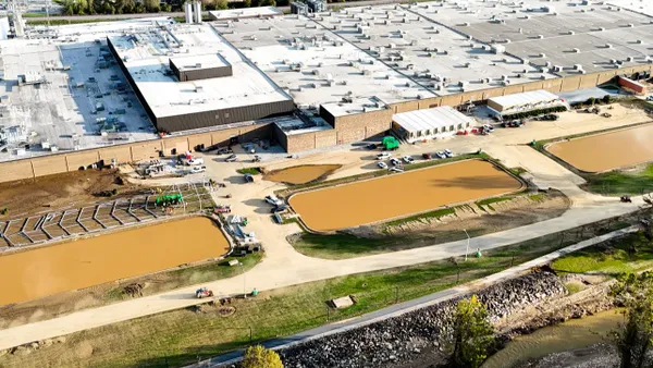 An overhead view of an industrial building affected by flooding, trucks and workers are on the ground in the surrounding area.