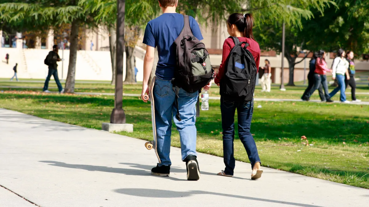 Two college students walk side by side down a campus sidewalk.