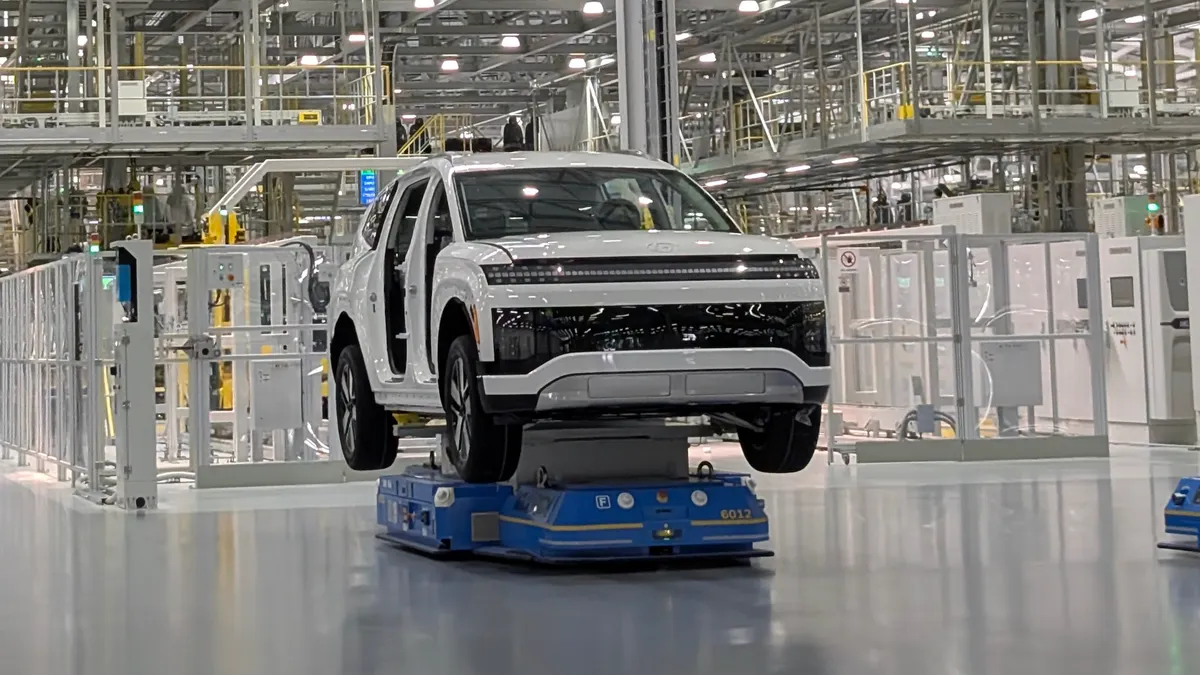 A white IONIQ 9 electric SUV being moved by an autonomous factory robot at Hyundai's Metaplant America in Georgia.