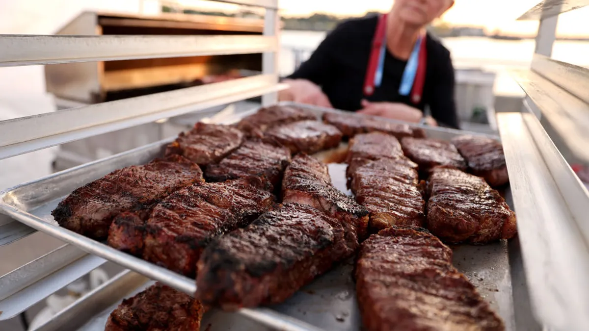 A woman pulls steak out of an industrial grill