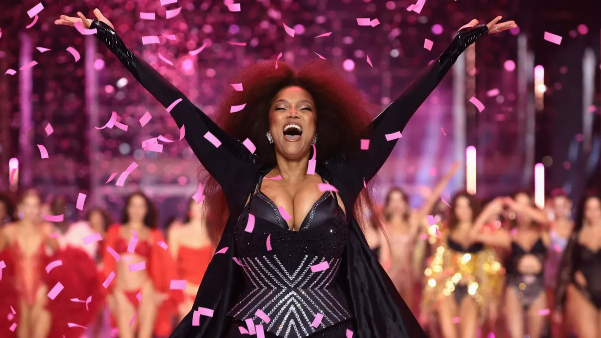 A person waves her arms in the air as confetti falls on a runway.