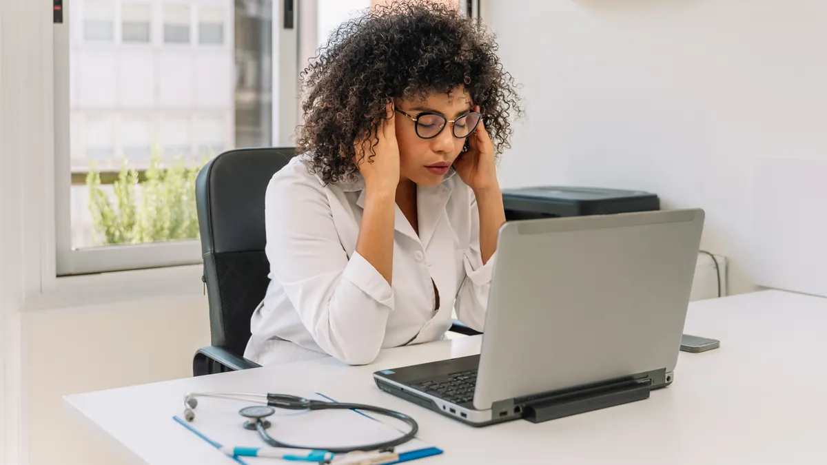 A woman sitting at a desk with her hands on her head, appearing stressed with everything life has thrown on her.