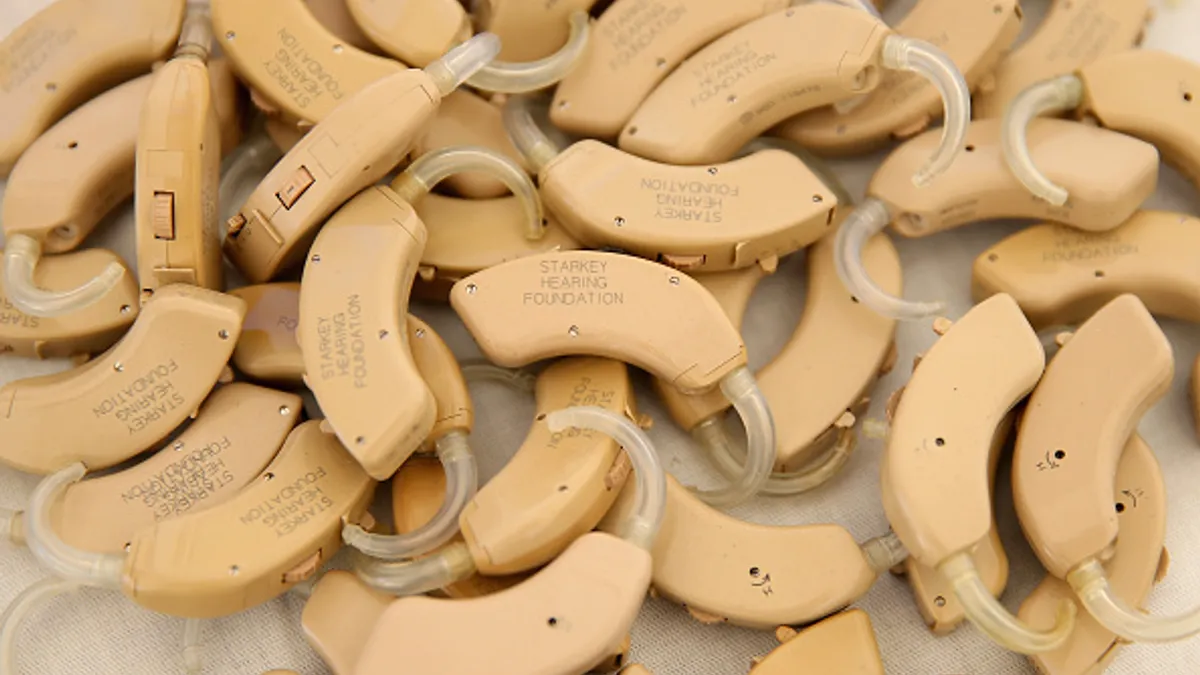 Several tan hearing aids with the words "Starkey Hearing Foundation" are piled up.