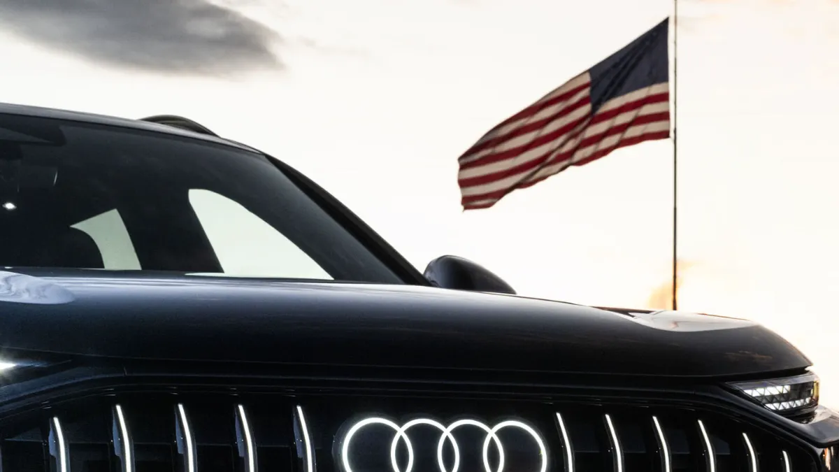 The grill of a black Audi SUV with an American flag on a pole in the background.