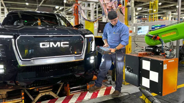 A worker on the assembly line at GM's Factory Zero EV plant in Michigan standing in front of a GMC Sierra electric pickup.