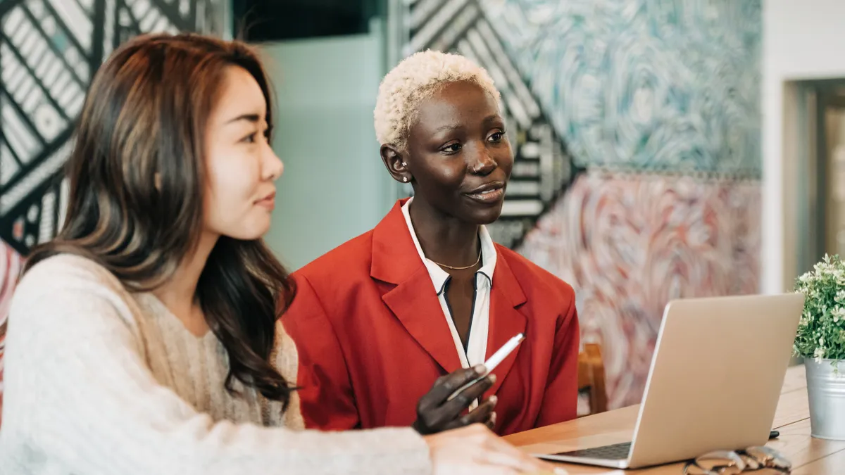 Two feminine-presenting people are talking in an office