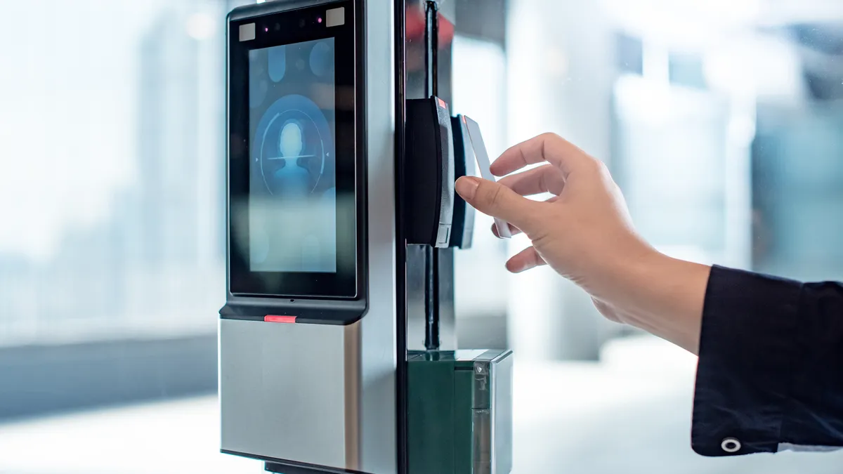 A male hand uses a key card to open a smart door lock for security systems on a glass door in an office building.