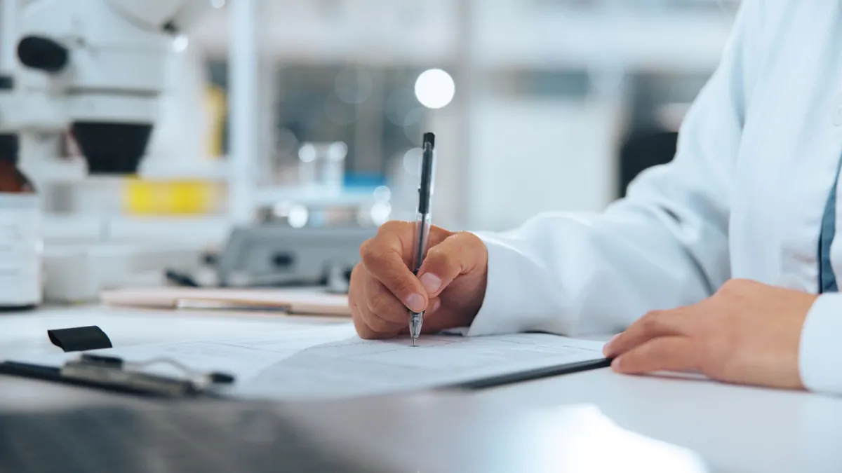 A close up of the hands of someone writing on a clipboard in a scientific laboratory.