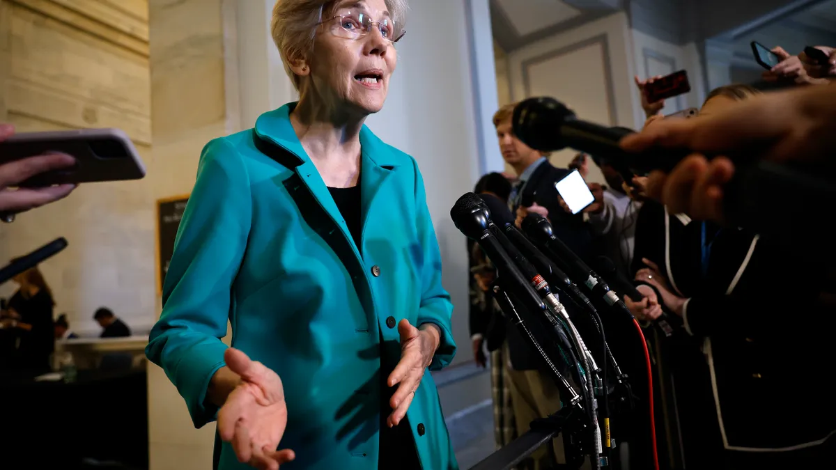 Elizabeth Warren speaks into microphones and cell phones while surrounded by reporters.