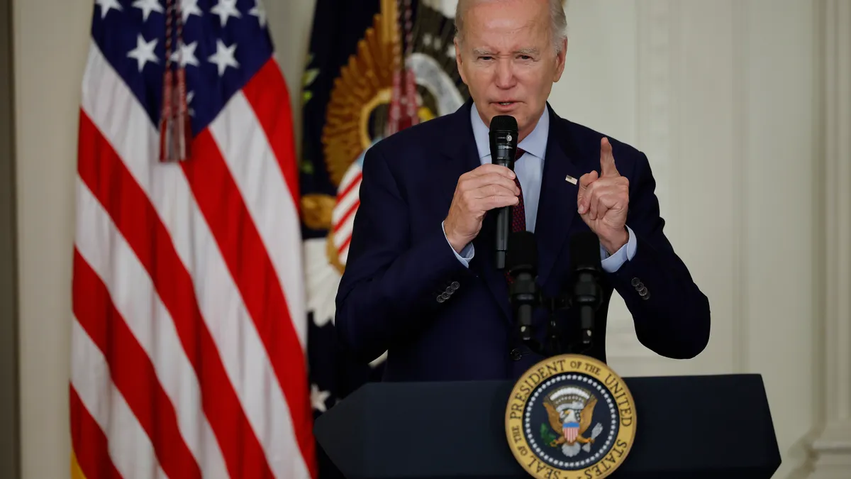 President Joe Biden holds a microphone in one hand and points a finger on his other hand