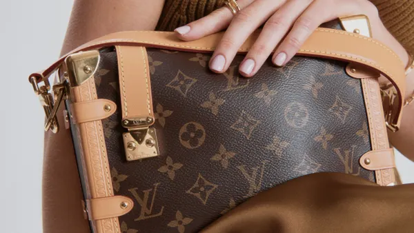 A person holds a Louis Vuitton handbag in a close-up view.
