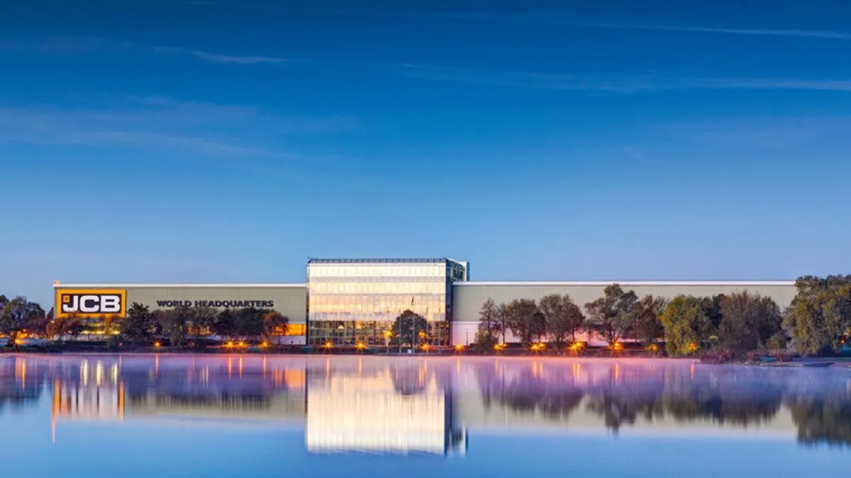 JCB's headquarters building with trees lined up across as well as a lake in front of it.