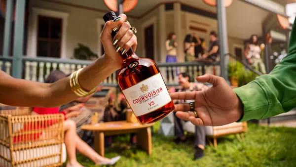 A bottle of Courvoisier is passed between two people, who are out of frame.