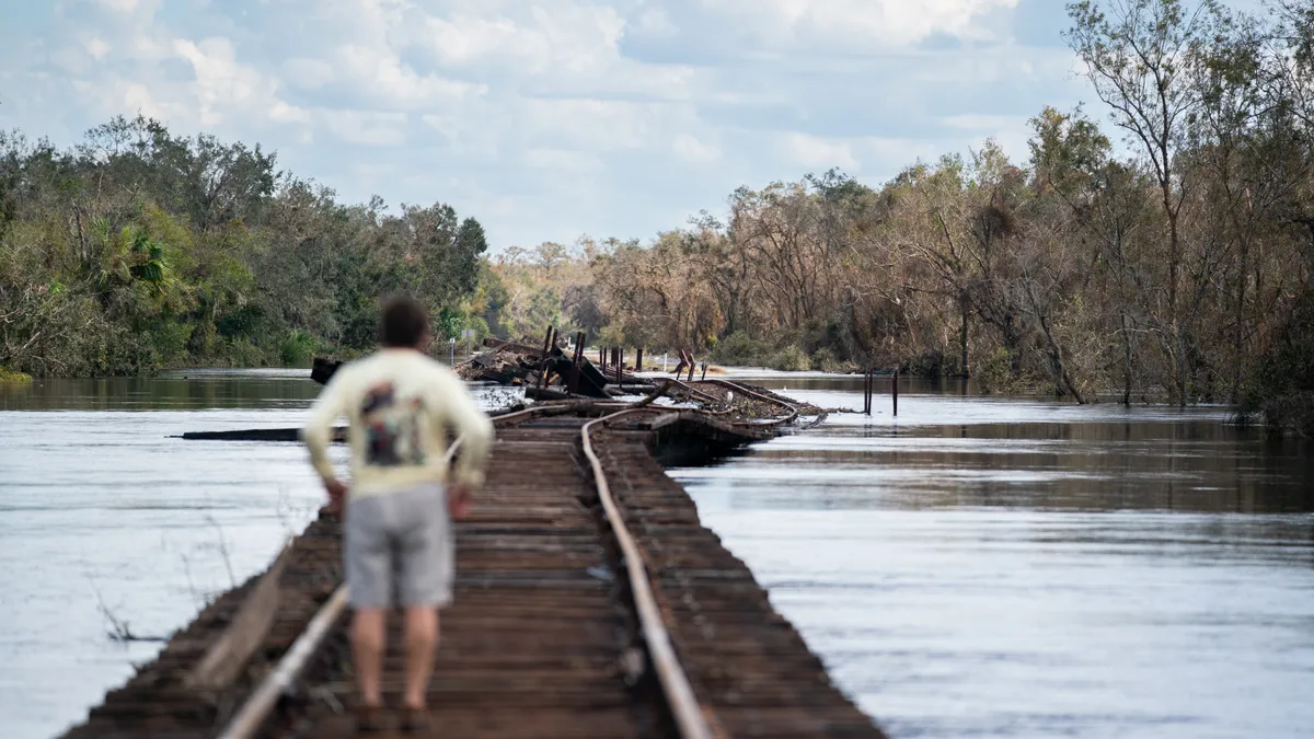 A man standing on railroad tracks is surrounded by water