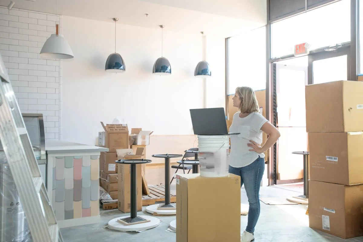 An image of a woman looking at an under construction shop with boxes around her.