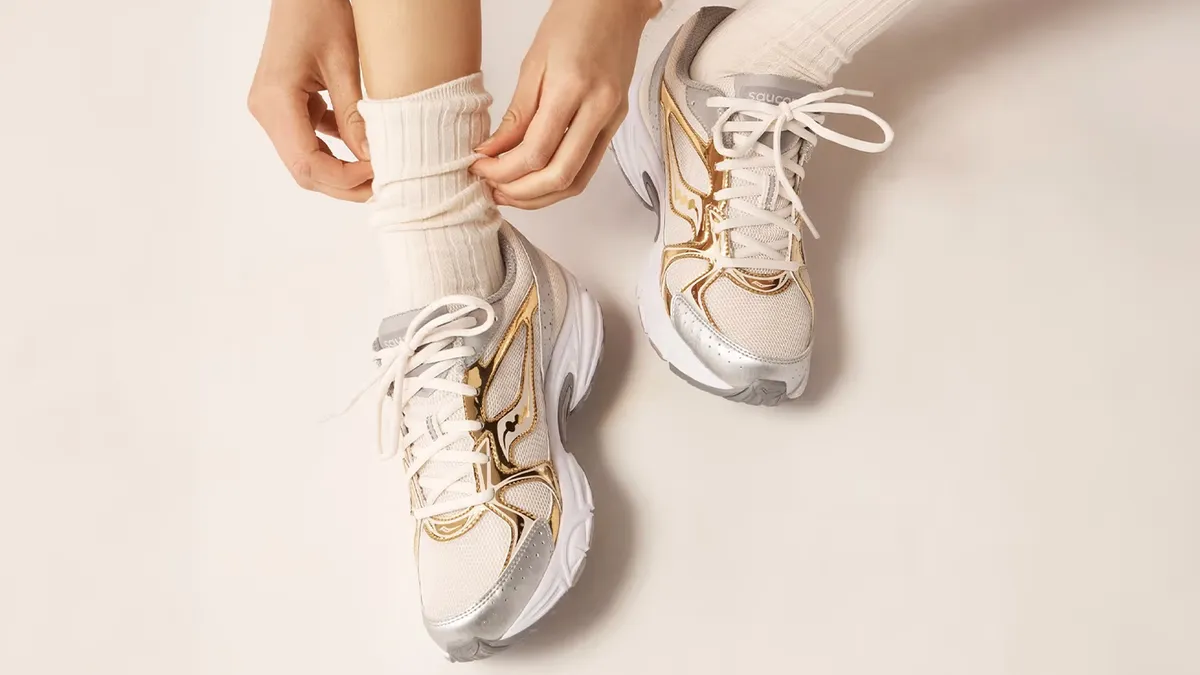 A close-up of a person tying a pair of white and gold sneakers.