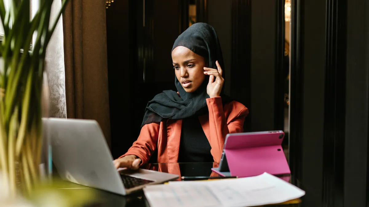 A hijabi person looks at their laptop in distress