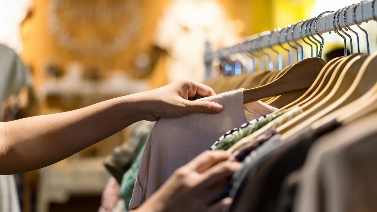 Close up of a person's arm reaching out to chose a t-shirt on a hanger off of a clothes rack.