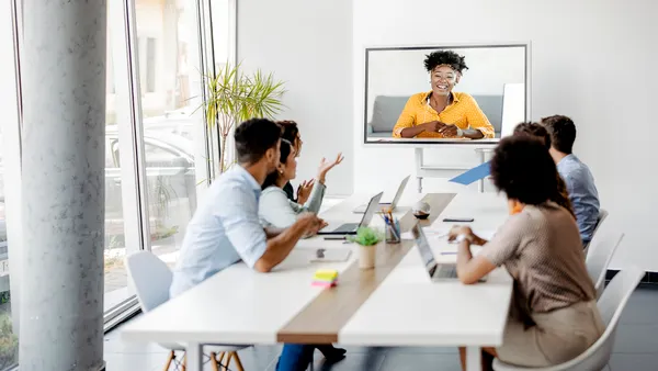 A group of employees in an office talking to another remote participant via collaboration technology.