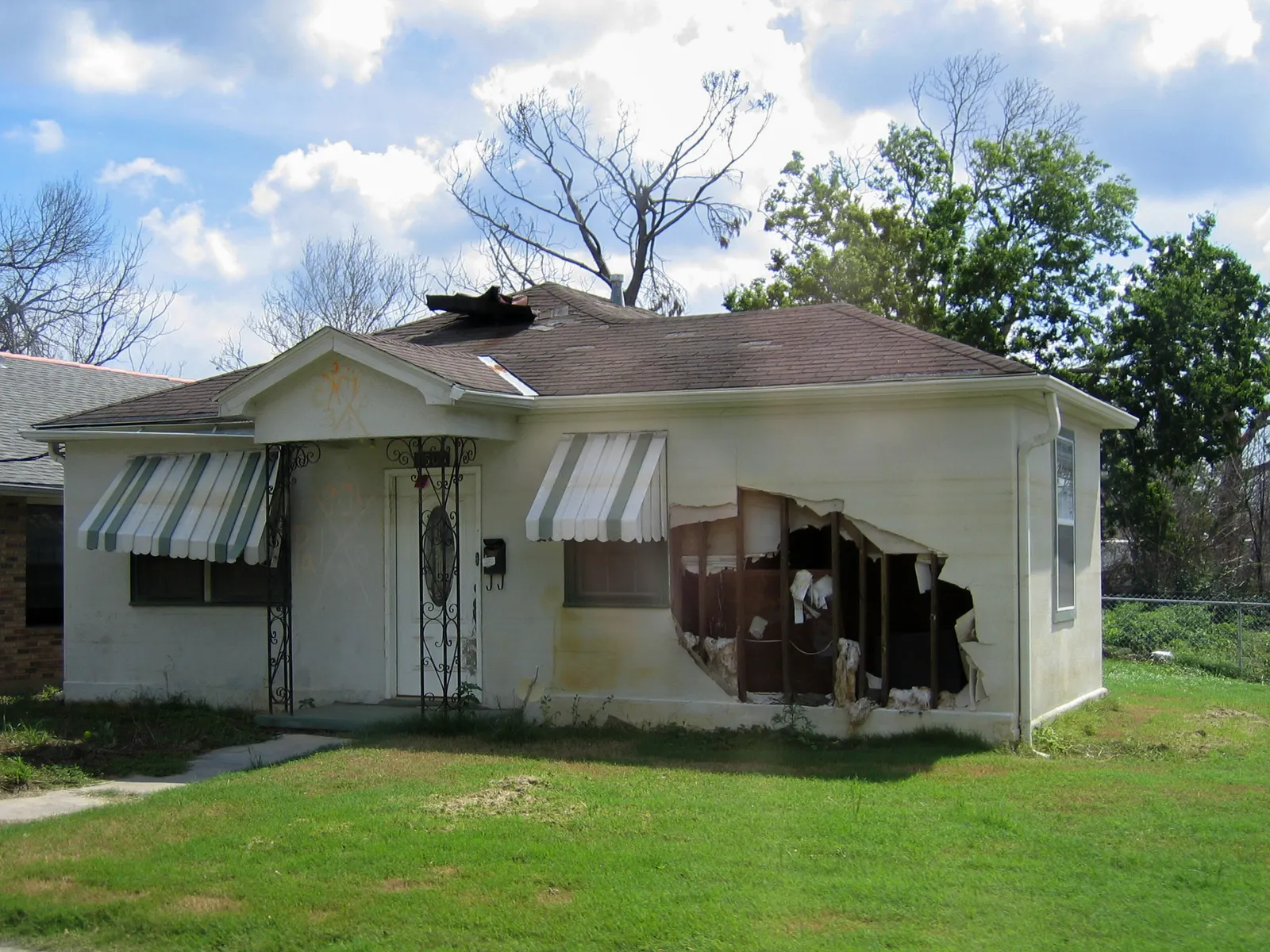 A small single-level home with a gaping hole in the front and damage to the roof.