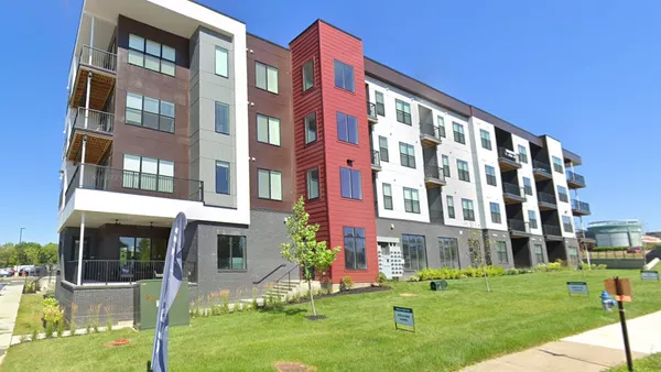 A mid-rise apartment building. Several flags and signs are on the lawn.