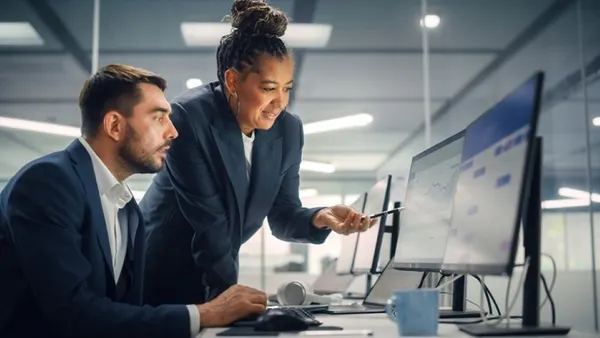 Two colleagues looking at a line chart on a monitor in an office.