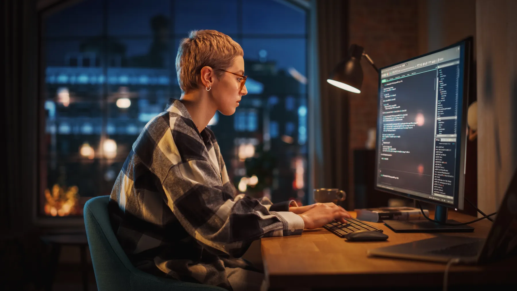 Young Woman Writing Code on Desktop Computer in Stylish Loft Apartment in the Evening.