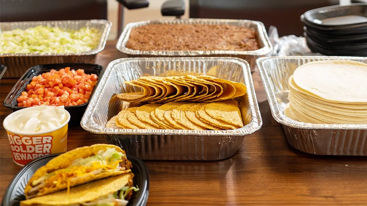 Trays of taco shells and other food in front of a sad banner that says welcome back to the office