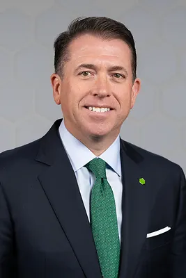 A person wearing a dark suit, light shirt and dark green tie smiles for the camera