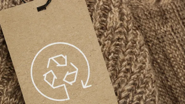 A brown recycling tage lies on top of a brown knit fabric.