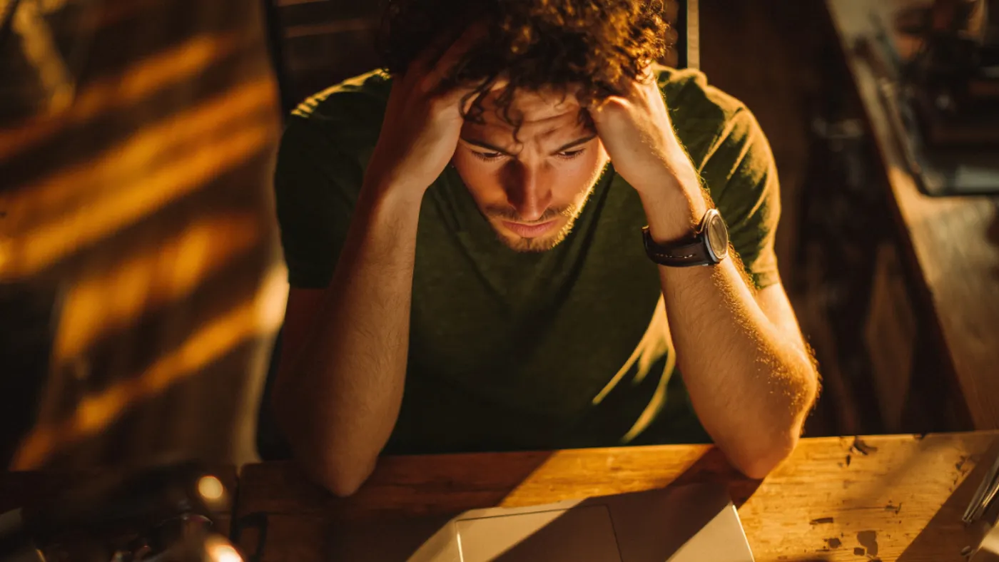 High angle shot of a person sitting at a desk with their hands on their head.