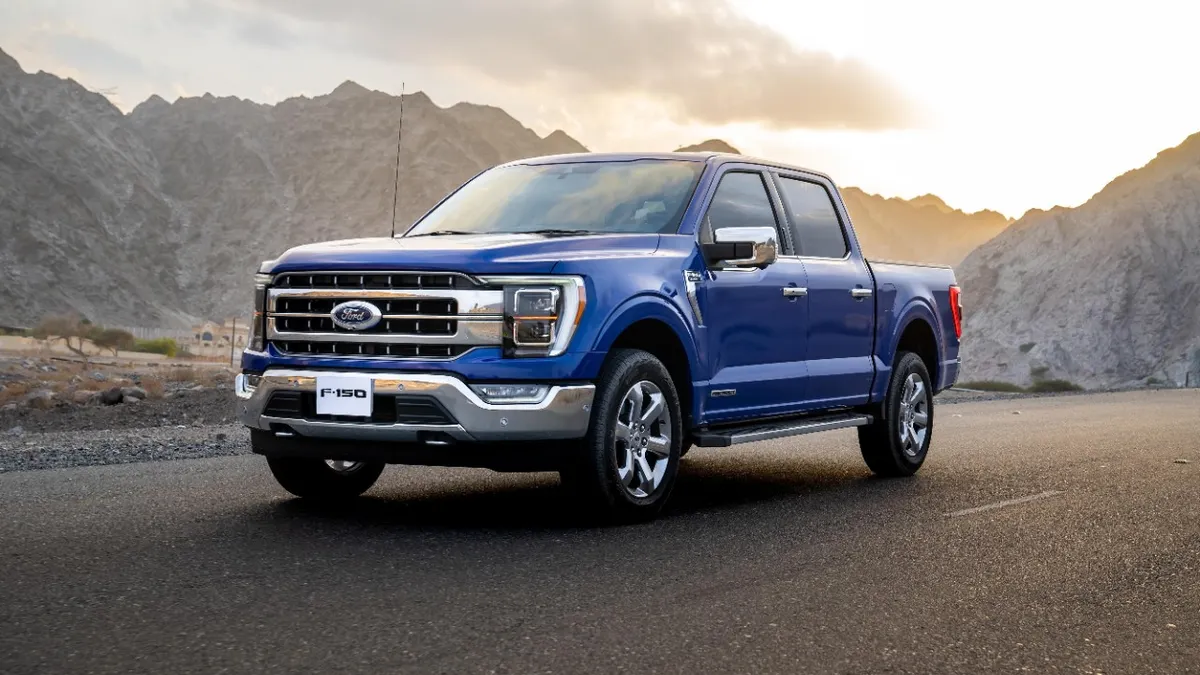 A blue 2021 Ford F-150 pickup on a road with mountains in the background.