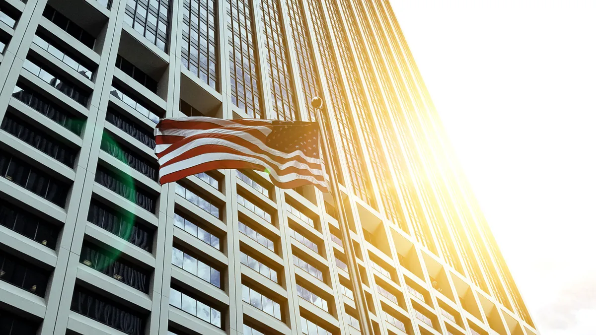 American flag in front of tall skyscraper building.