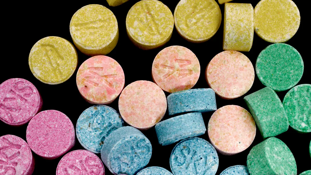 Multicolored pills of MDMA bearing the word "Sky" are arranged against a black background.
