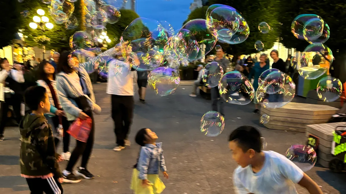 People look up at bubbles floating across a city street.