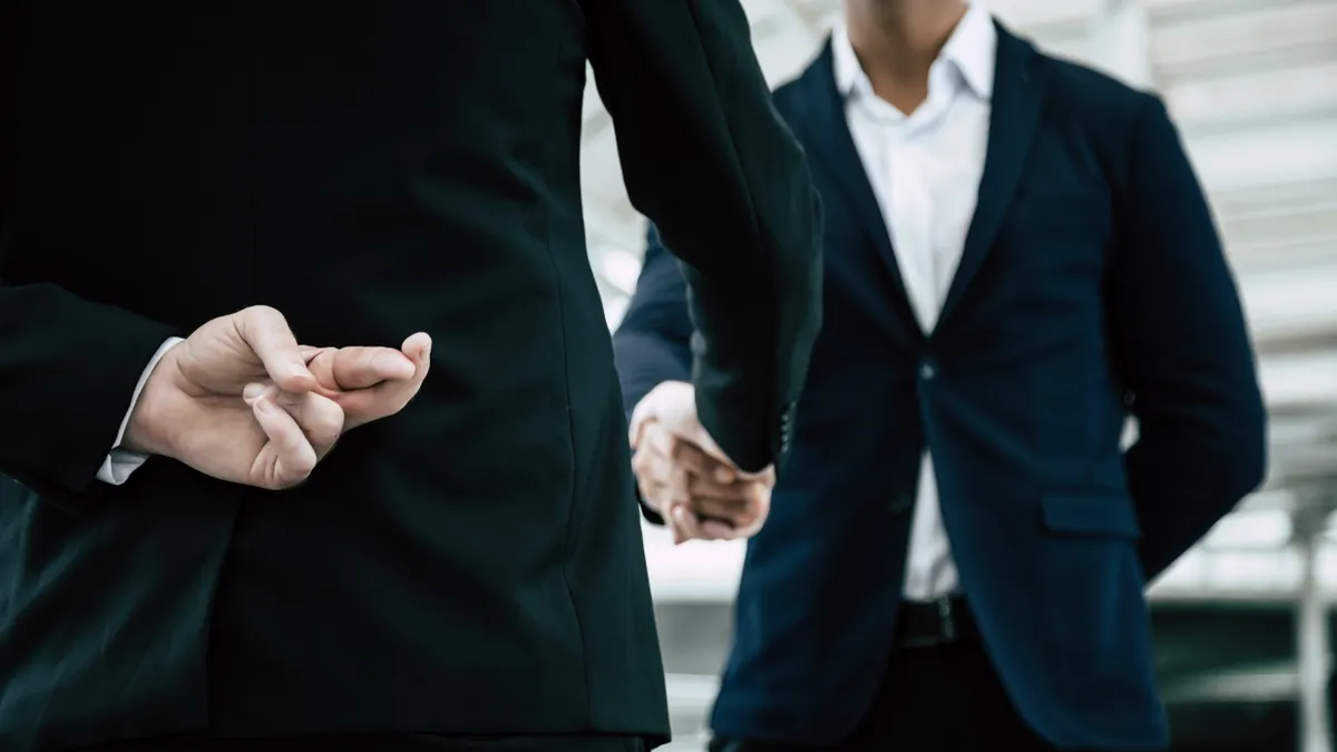 Businessman crosses his fingers behind his back during a handshake.