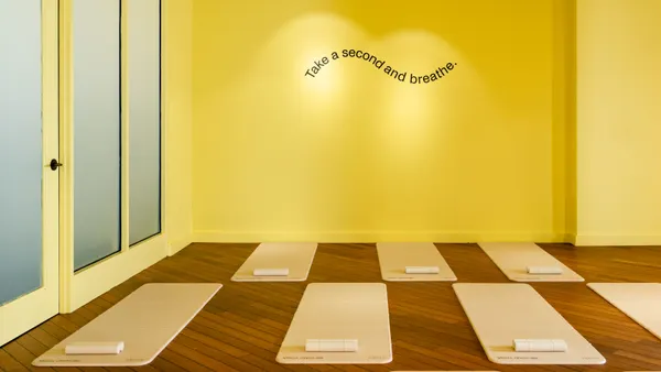 A yellow room outfitted with yoga mats, with "take a second and breathe" on the wall.