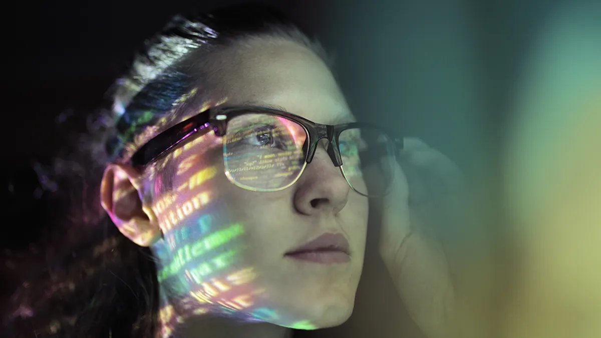 A person with glasses on and the glasses reflection showing code