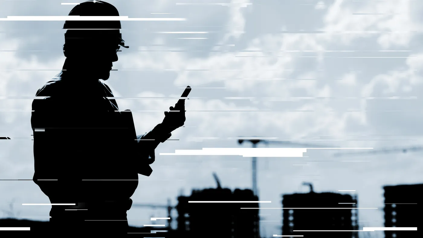 A silhouette of a person wearing a construction hat and holding a phone, buildings are seen in the background. The image is glitched.