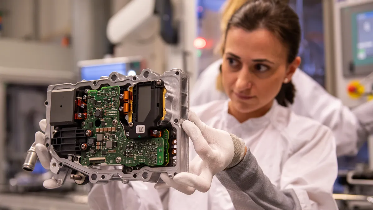 Image shows a technician holding up and examining an electronic part.