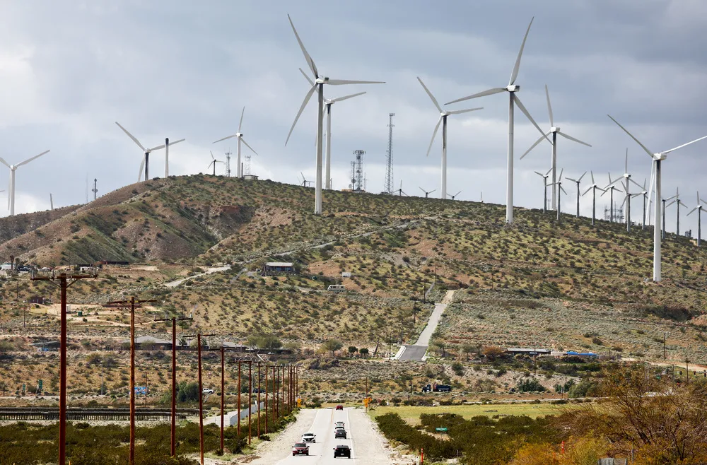 Wind turbines operate at a wind farm in Coachella Valley, as vehicles drive on a highway below.