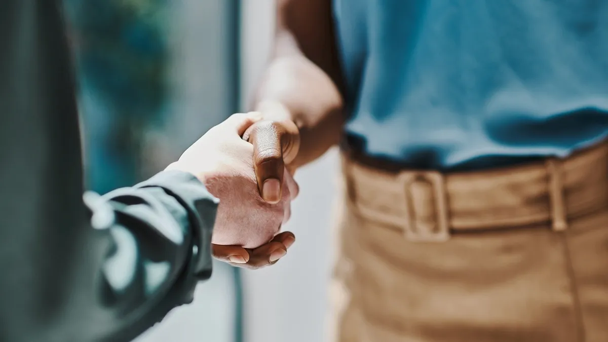 A White hand and a Black hand shake in the office