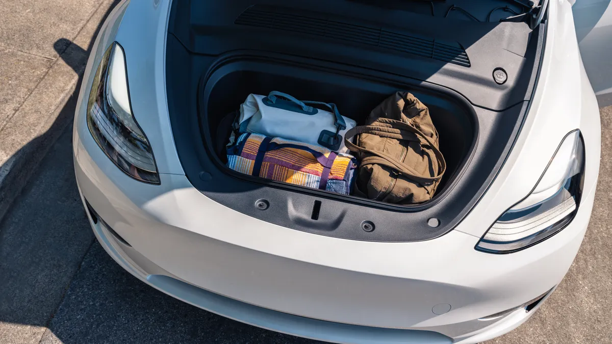 An overhead view of the front storage compartment of a white Tesla model Y with duffle bags stored inside.