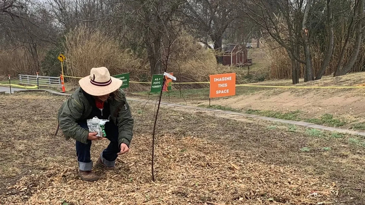 A person holding a bag crouches next to a small planting in front of signs that read "Imagine this space"